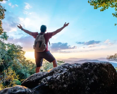 Rear view back of Young asian hiking man standing and rise-up hands with happy on peak of rocky mountain, copy space